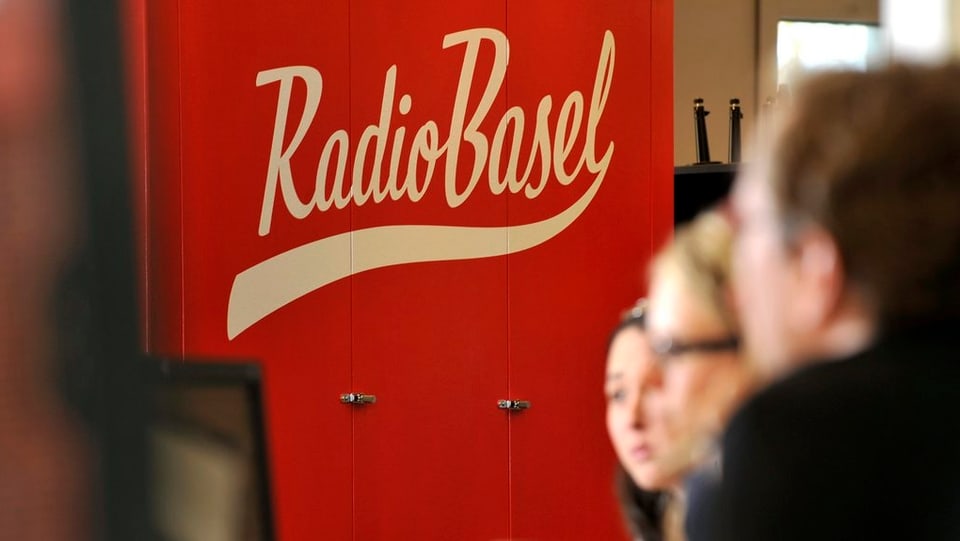 Mehrere Personen an einer Sitzung vor dem Radio Basel Logo
