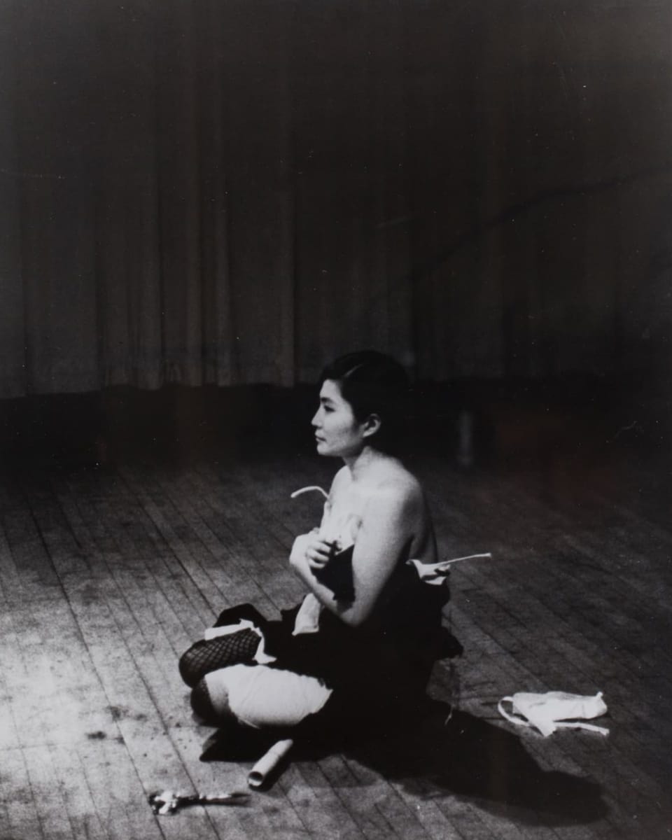 Die Künstlerin Yoko Ono sitzt fast nackt auf dem Boden.