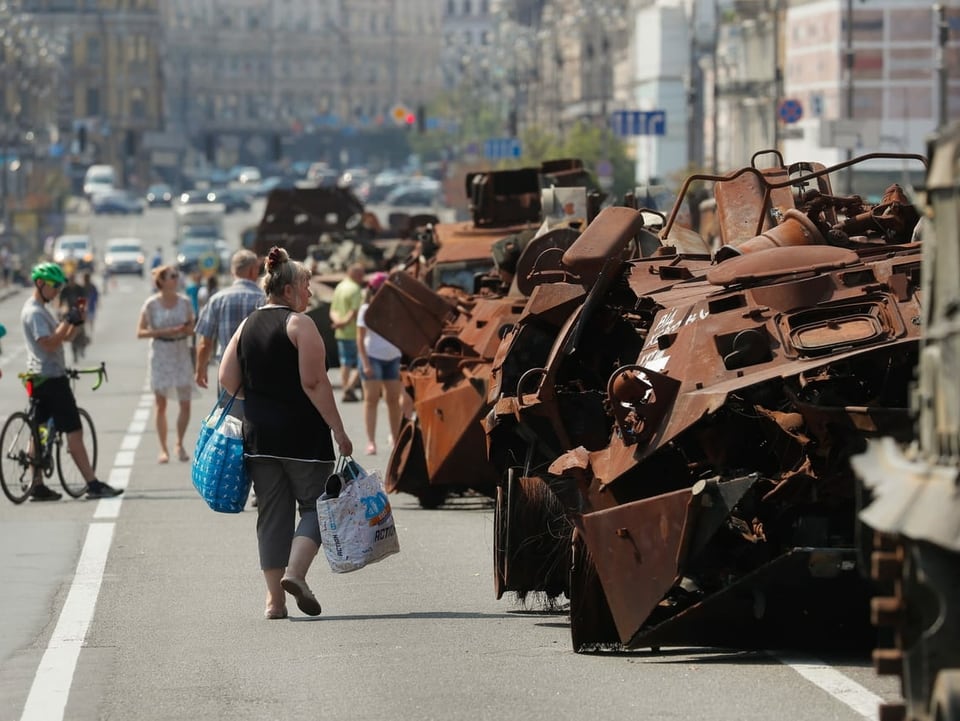 Menschen gehen an beschädigten russischen Militärpanzern vorbei.