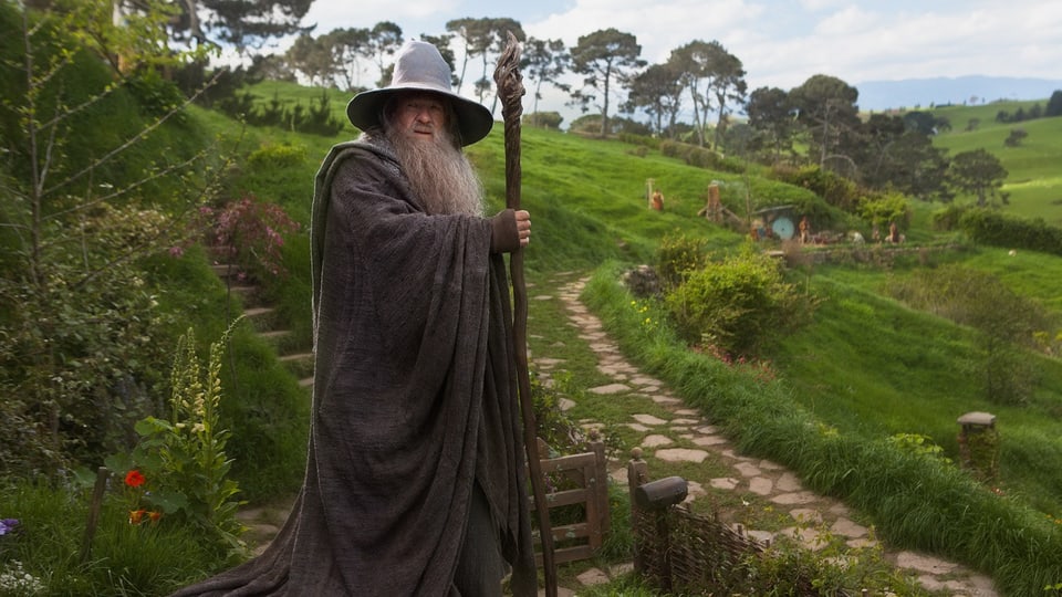 Der Zauberer Gandals steht im Auenland vor einem grasigen Hügel. 