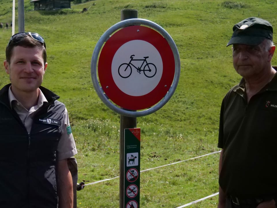 Zwei Männer vor einer Verbotstafel für Biker.