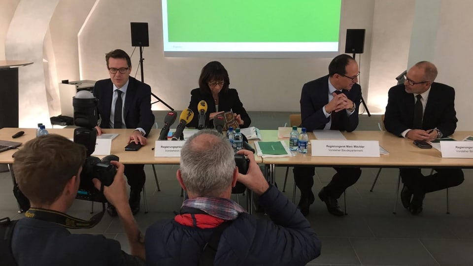 Die vier Regierungsmitglieder sitzen am Tisch. Fotografen lichten sie ab. 