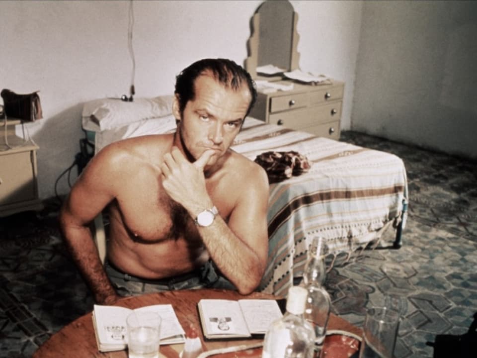Jack Nicholson sitzt mit nacktem Oberkörper in einem Zimmer.