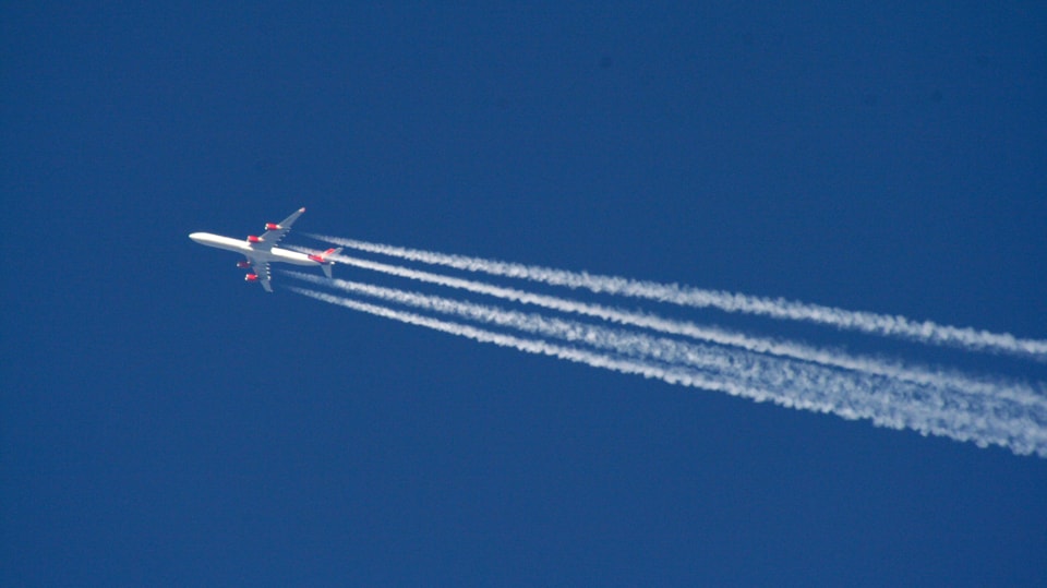 Blick auf Flugzeug vor blauem Himmel. Dahinter bilden sich Kondensstreifen.