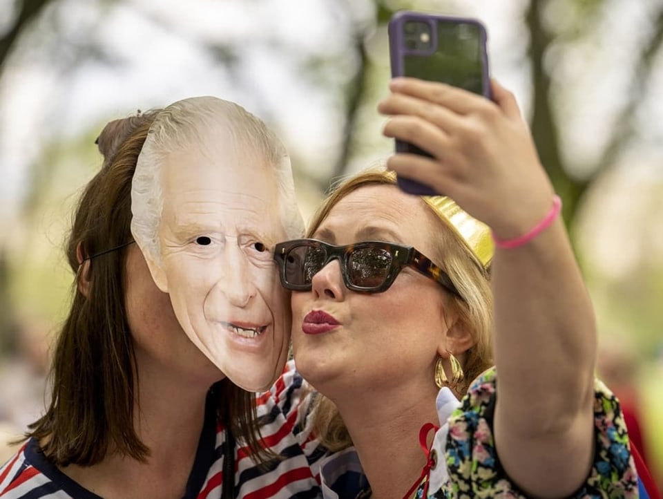 Zwei Frauen – eine mit einer König-Charles-Maske – posieren für ein Selfie