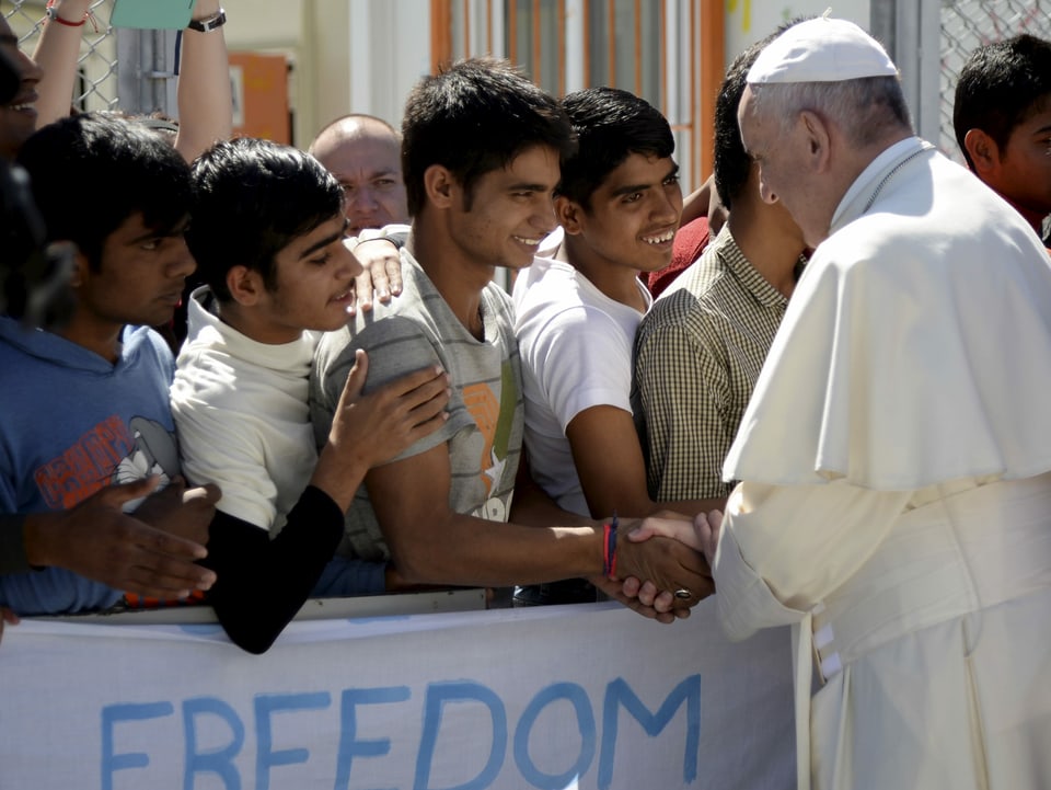 Eine Reihe von Männern steht hinter einer Absperrung; vor ihnen der Papst. Ein erster schüttelt dessen Hand.
