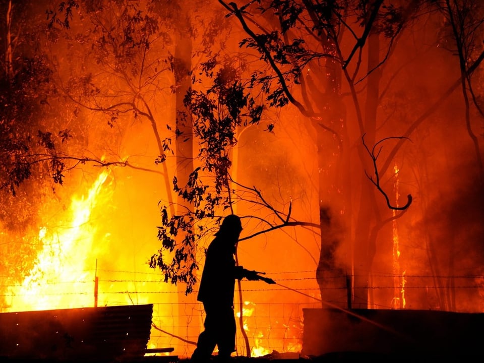 Die Silhouette eines Feuerwehrmanns vor Flammen (keystone)