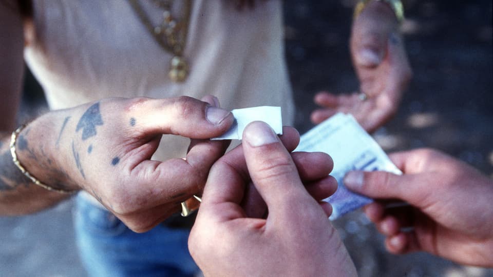 Die Hände eines Drogendealers beliefern die Hände eines Kunden mit Drogen gegen Geld (Symbolbild)