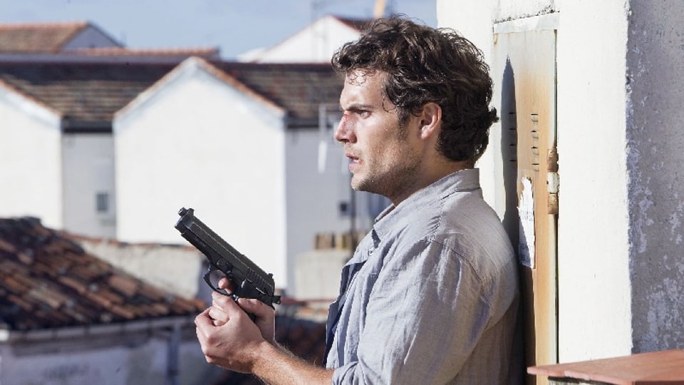 Ein Mann steht an der Wand eines Hauses mit einer Waffe in der Hand.