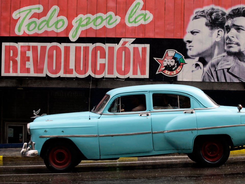 Ein altes Auto auf Kuba vor einer Wand mit dem Gesicht Fidel Castros