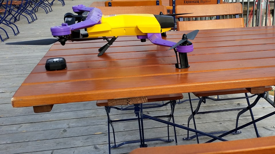 Das Bild zeigt die gelb-violette Airdog-Drohne (Quardocopter) auf einem Tisch des Bergrestaurants Tschentenalp.