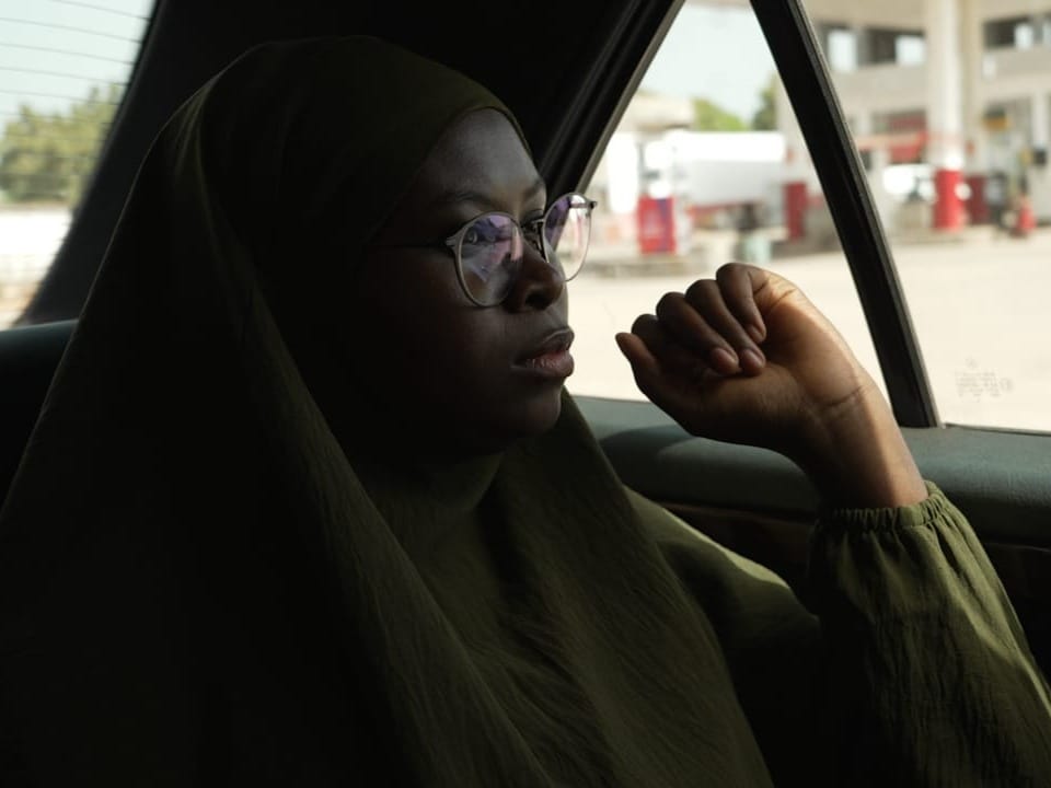 Fatoumatta Sandeng, eine junge gambische Frau sitzt im Rücksitz eines Autos. Sie starrt gedankenverloren in die Ferne. 