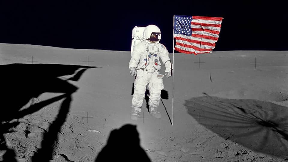 Edgar Mitchell im Raumanzug auf dem Mond neben einer US-Flagge