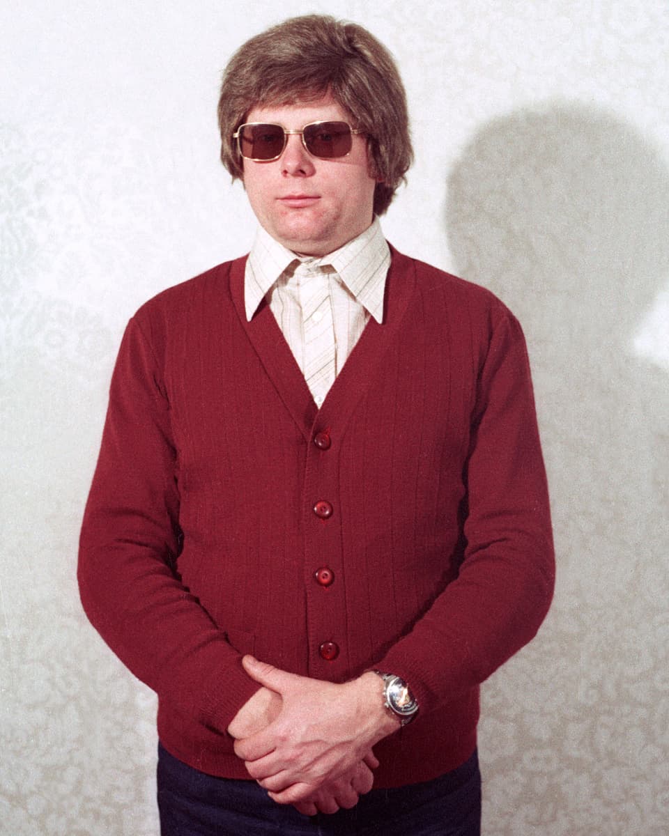 Ein Mann mit rotem Pullover, Perücke und Sonnenbrille.