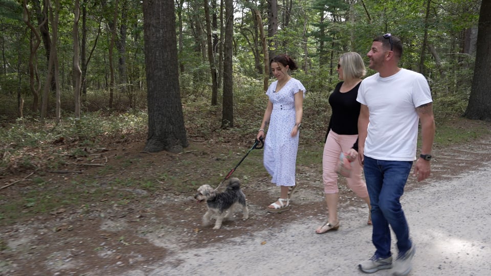 Alexis, ihr Assistenzhund und die Eltern von Alexis spazieren im Wald.
