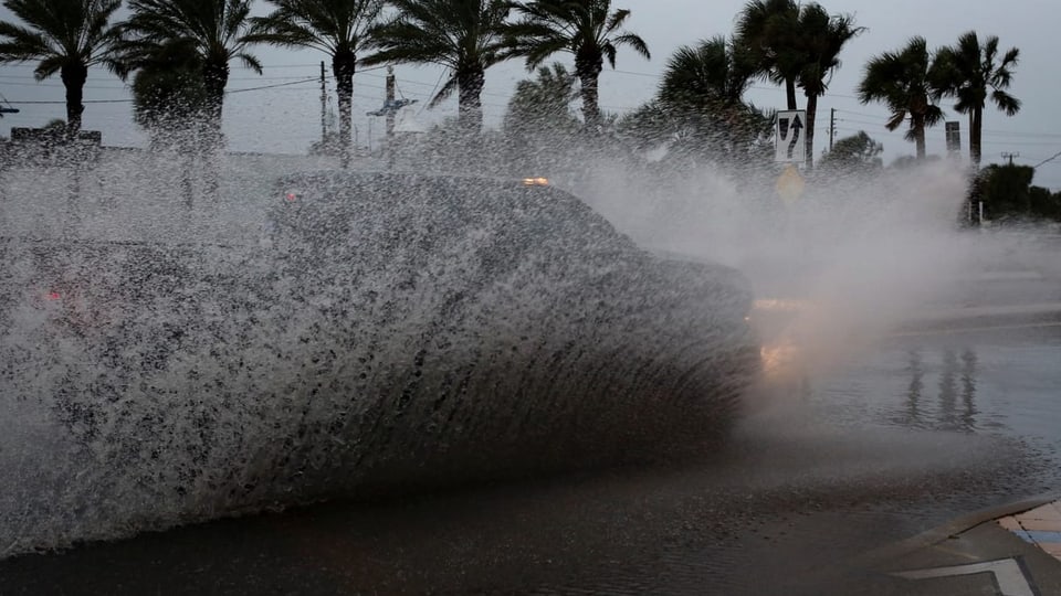 Eine Auto fährt durch eine Pfütze und wirft Wasser auf. 