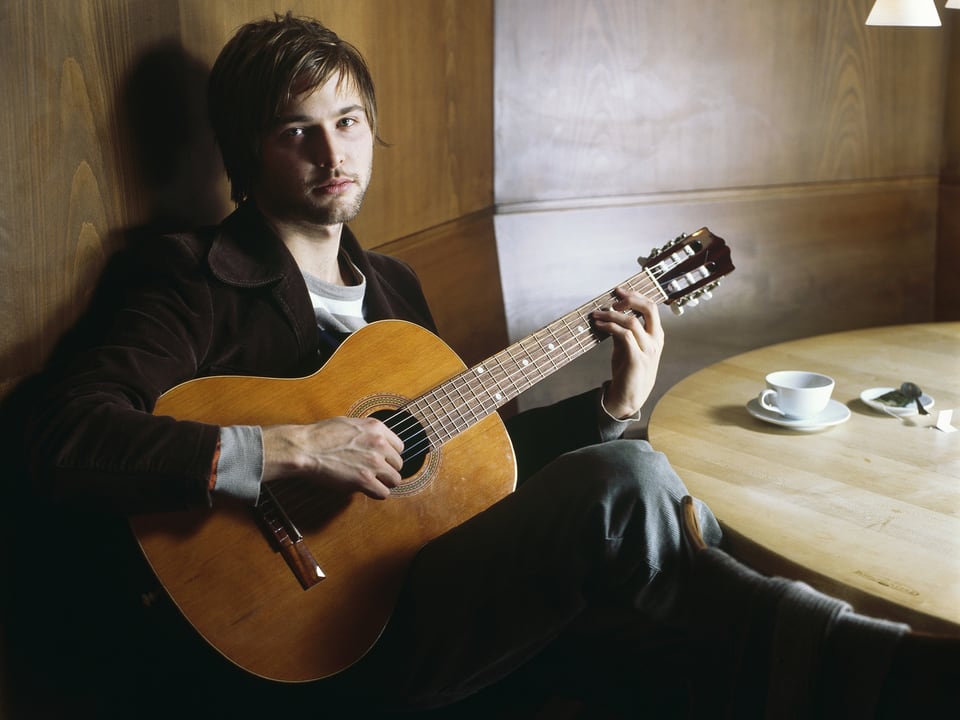 Portrait Nils Althaus mit Gitarre in einer Beiz an rundem Tisch.