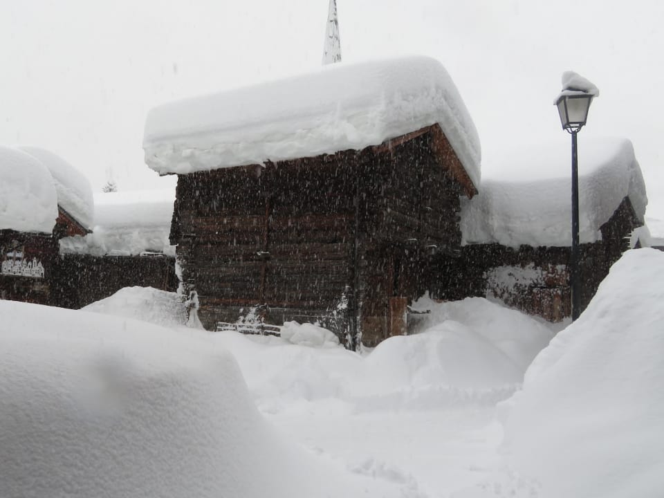 Dorf mit Holzhäusern und meterhoch Neuschnee in den Gassen und auf den Dächern