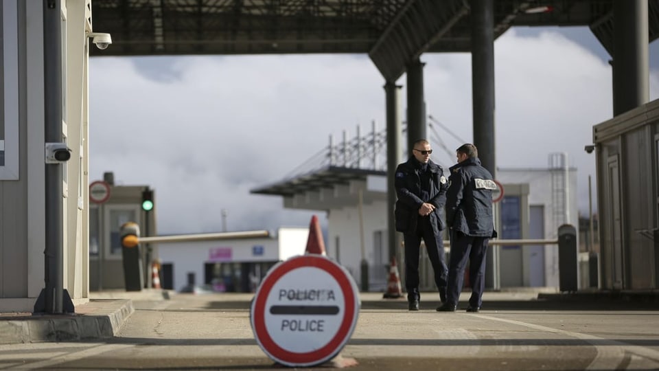 Zwei Polizisten stehen am Grenzübergang. Davor ein Schild mit der Aufschrift «Police».