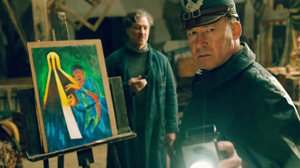 Filmstill: Ein Maler im Atelier, im Vordergrund ein Polizist mit Taschenlampe.