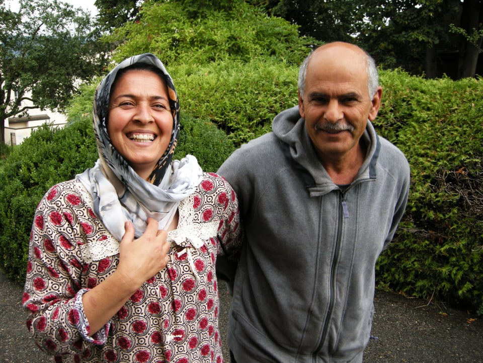 Eine Frau und ein Mann stehen lachend in einem Garten.