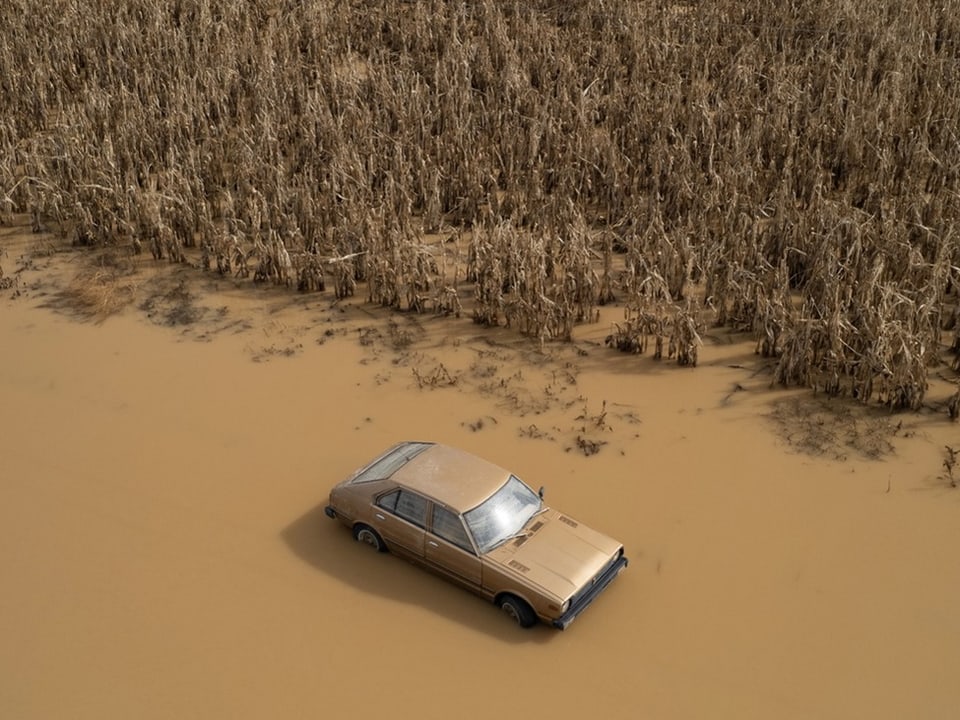 Ein Auto inmitten der Wasserfluten neben einem Kornfeld.