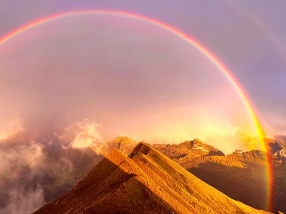 Berggrat mit Regenbogen und ein paar Wolken bei Sonnenuntergang