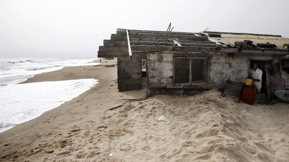 Das Haus ist bis zur Hälfte im Sand eingesunken und die Wellen kommen schon bedrohlich nahe.