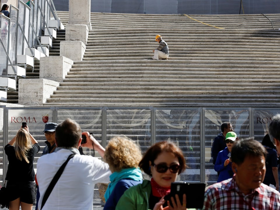 Touristen vor einer Glasabschrankung. Im Hintergrund ein Arbeiter auf der Spanischen Treppe.
