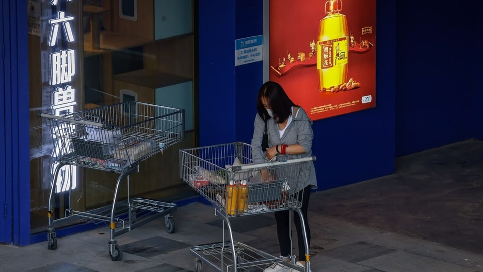 Eine Frau steht neben einem silbernen Einkaufswagen. Daneben eine rote Reklame mit chinesischen Schriftzeichen