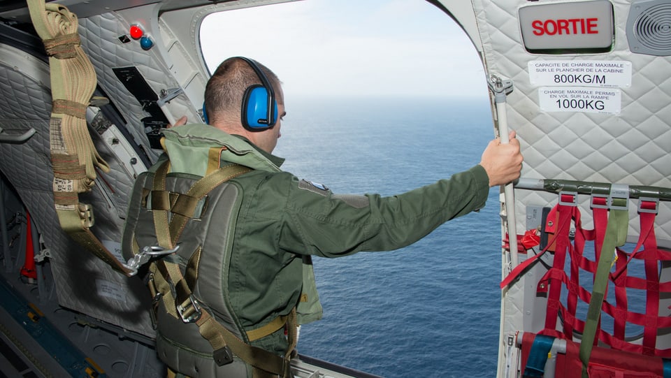 Ein Soldat blickt aus einer geöffneten Flugzeugtüre auf das Meer.