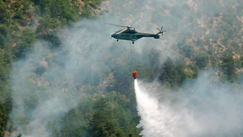 Helikopter wirft Wasser auf rauchnenden Wald ab.