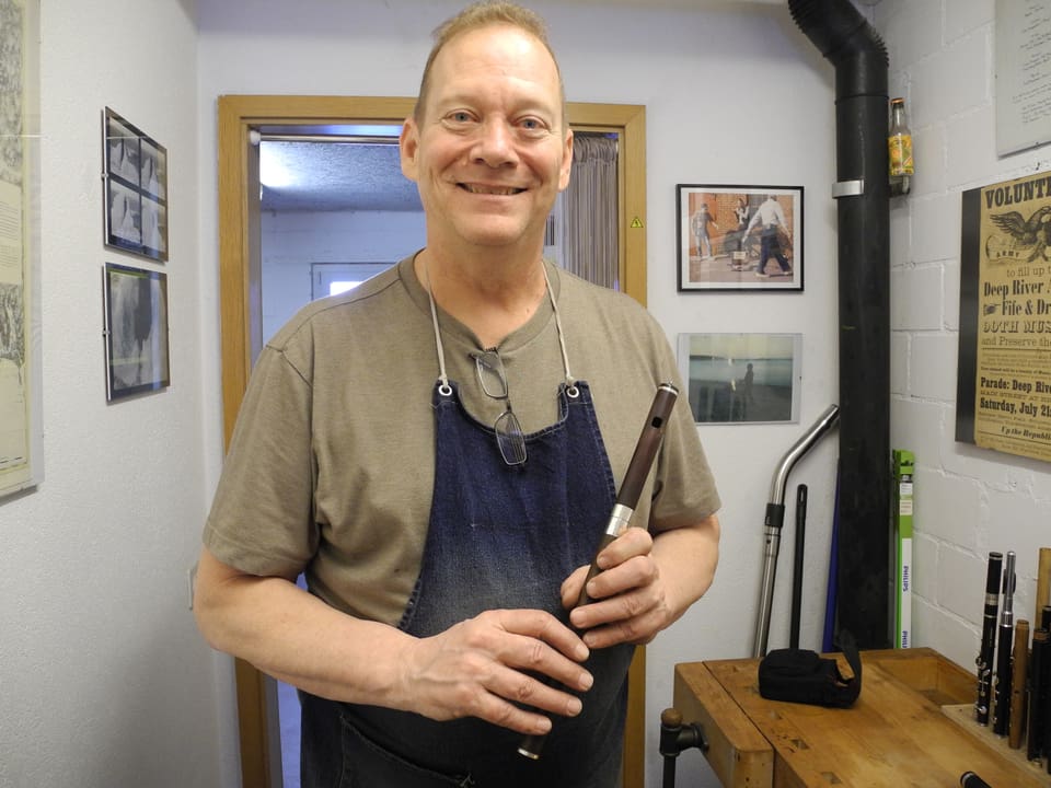 Flötenbauer Skip Healy mit Arbeitsschürze und fertiger Flöte in der Hand