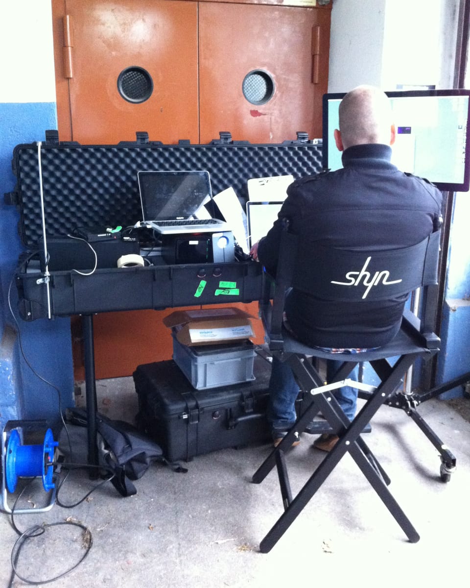 Ein Mann sitzt vor einem mobilen Arbeitsplatz mit Bildschirm, Computern und vielen Kisten.