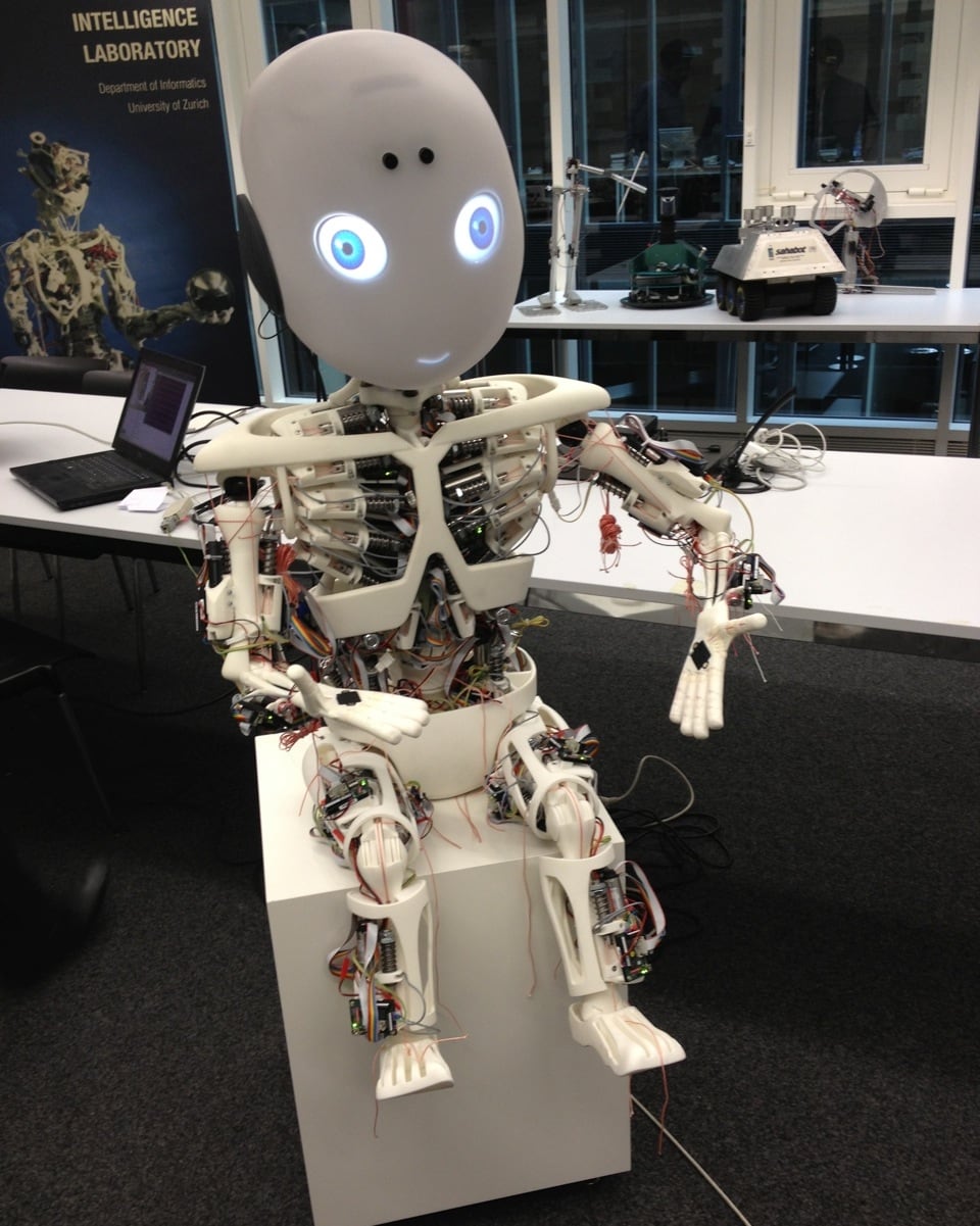 Roboter Roboy sitzt «strahlend» auf einem Hocker.