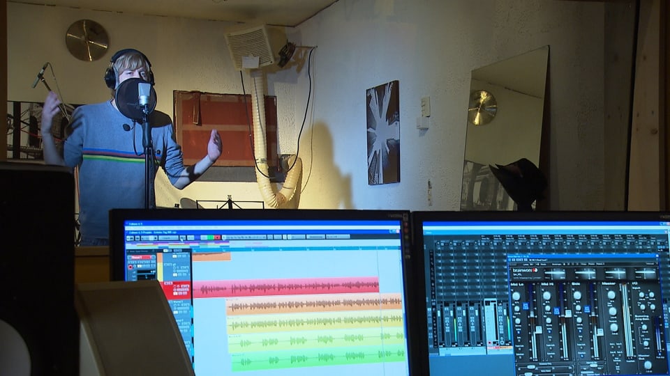 Massai am Mikrofon am singen, im Vordergrund sind zwei Computerbildschirme.