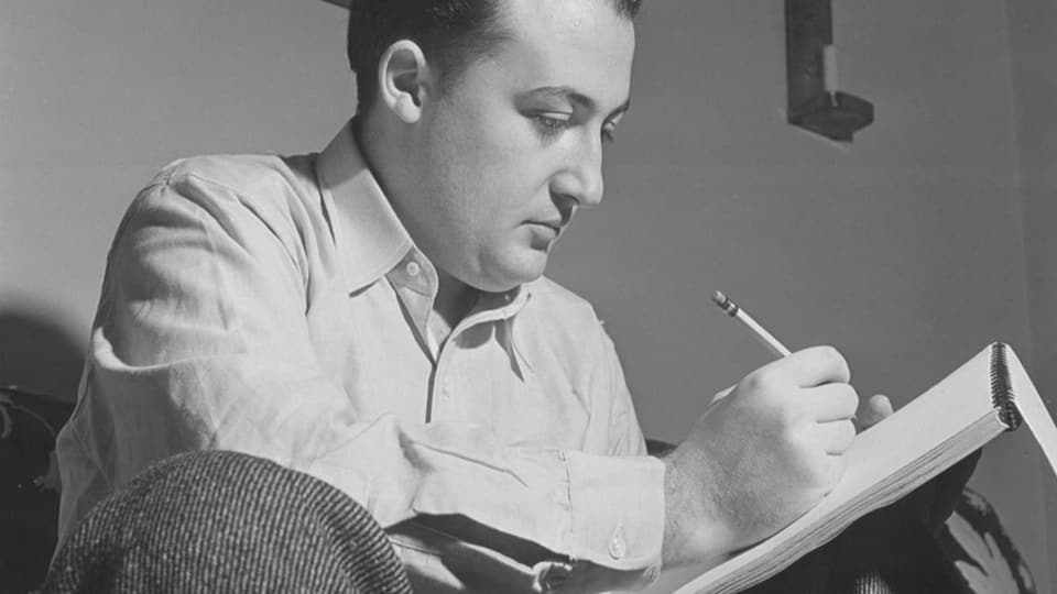 Schwarzweiss-Foto eines Mannes mittleren Alters, sitzt mit Skizzenbuch auf dem Bein, Stift in der Hand