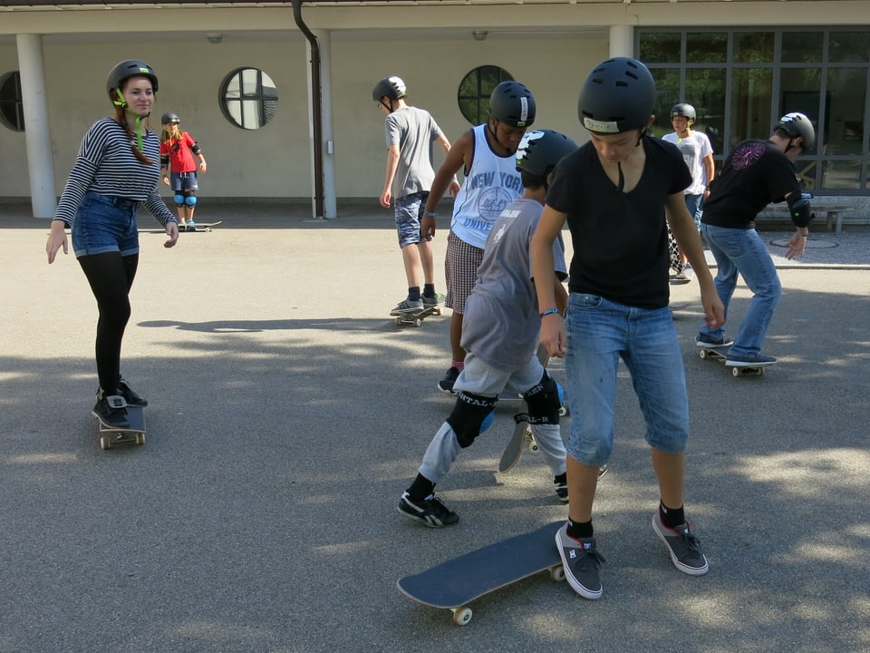 Jugendliche auf einem Pausenplatz mit Skateboards.