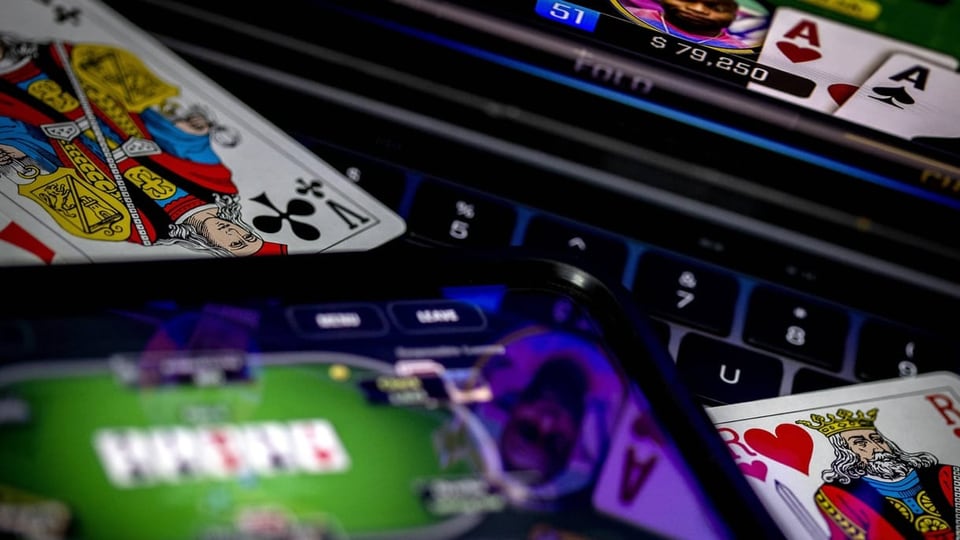 Online-Casino auf einem Handy und einem Laptop, daneben liegen Spielkarten