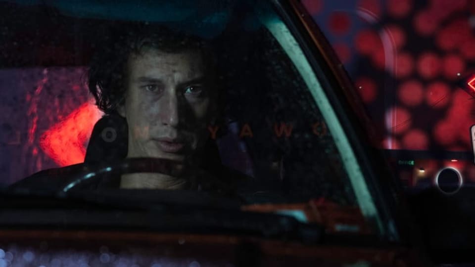 Adam Driver sitzt als Hauptdarsteller von «White Noise» am Steuer seines Autos, das vor einem Hotel steht.