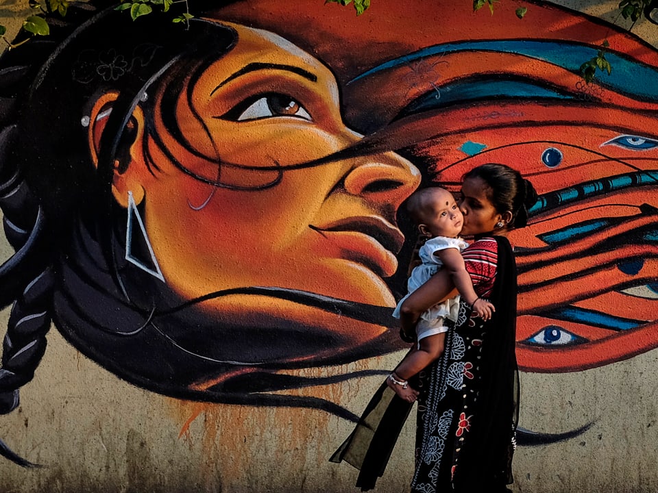 Mutter mit Baby vor einer Wandmalerei in Mumbay.