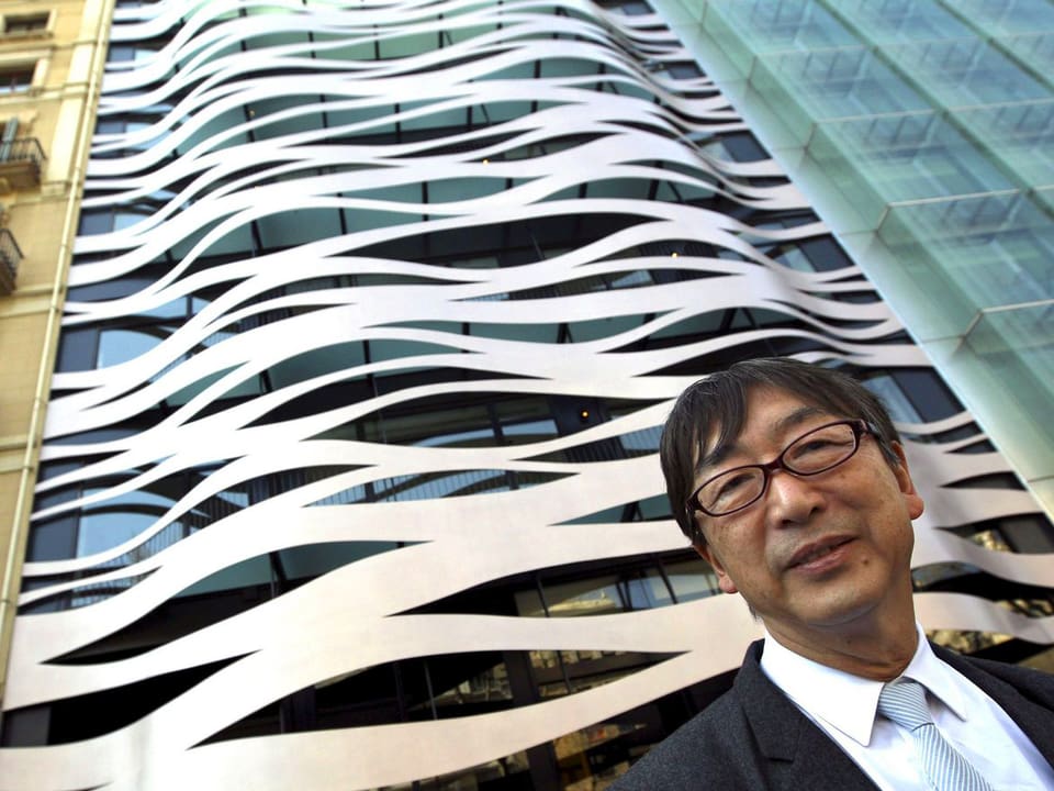 Kopf von Toyo Ito vor der weiss-gewellten Fassade eines Hochhauses.