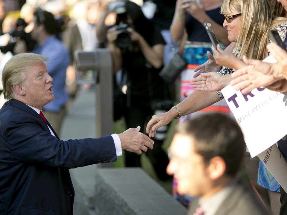 Trump gibt einer Anhängerin auf der Strasse die Hand.