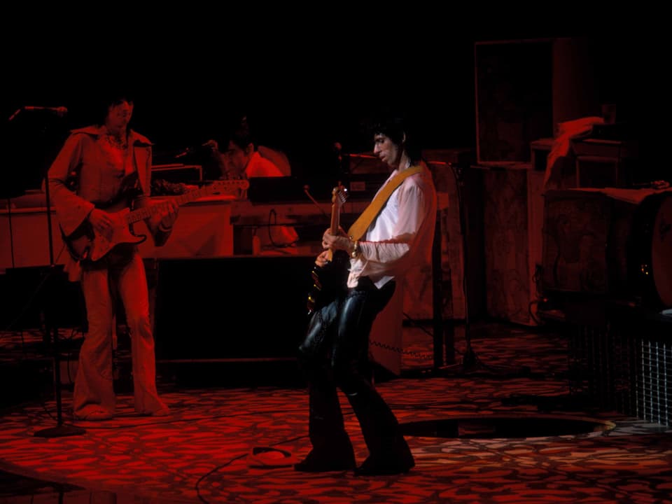 Zwei Männer spielen Gitarre vor rotem Hintergrund