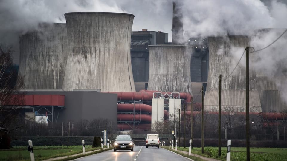 Eine Strasse führt zum Kraftwerk. Fünf Hochhaus-grosse Beton-Säulen ragen in die Höhe, darüber schwebt weisser Dampf.