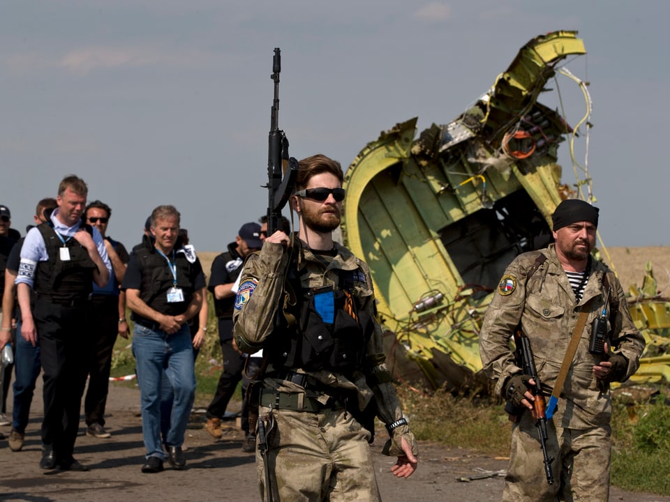 Im Vordergrund bewaffnete pro-russische Rebellen, im Hintergrund das Wrack der in der Ostukraine abgestürzten Maschine von Malysian Airlines sowie eine Delegation von Ermittlern und OSZE-Mitarbeitern.