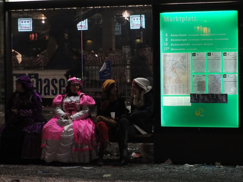 Frau in rosa Kostüm neben grünem Billetautomaten auf dem Marktplatz.