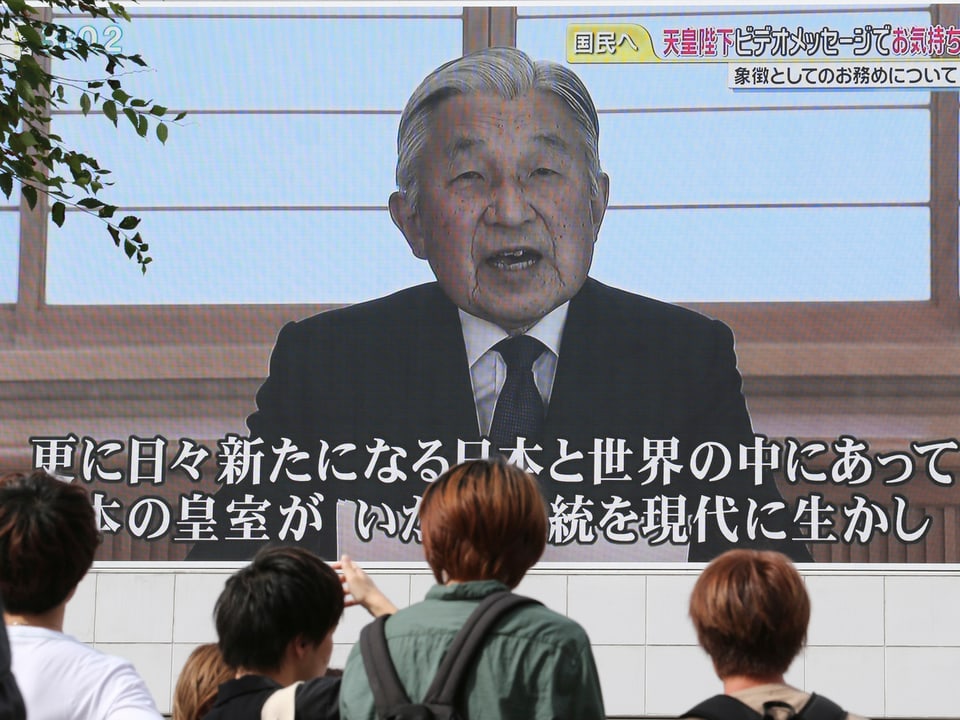 Menschen verfolgen die Akihitos TV-Ansprache vor einer grossen Leinwand.