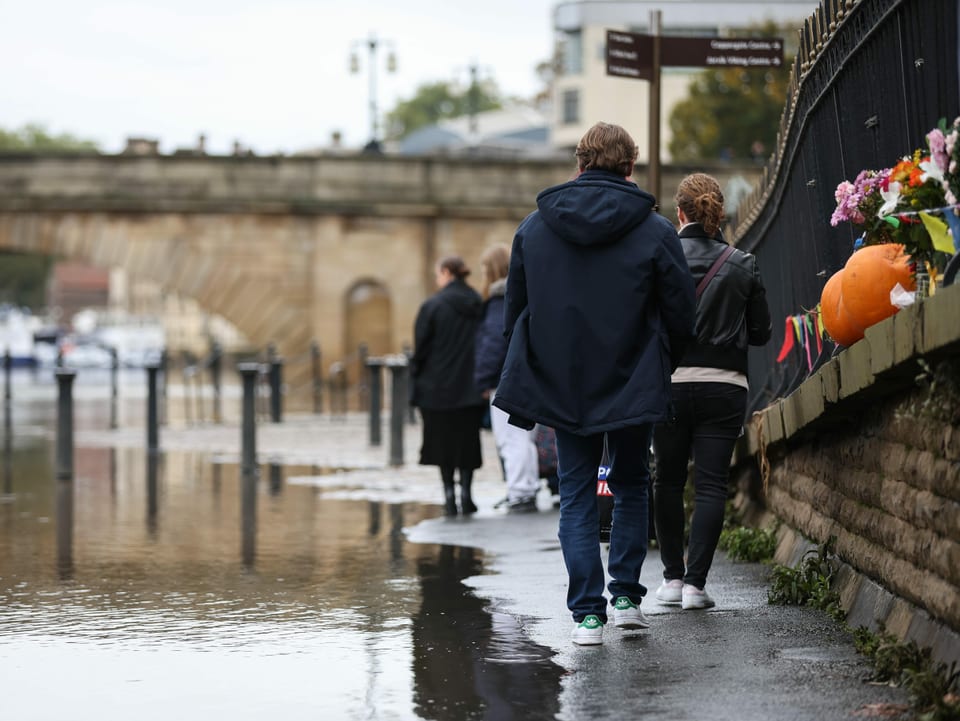 Menschen laufen auf einem Trottoir ganz aussen, weil die Mitte von Wasser überflutet ist.