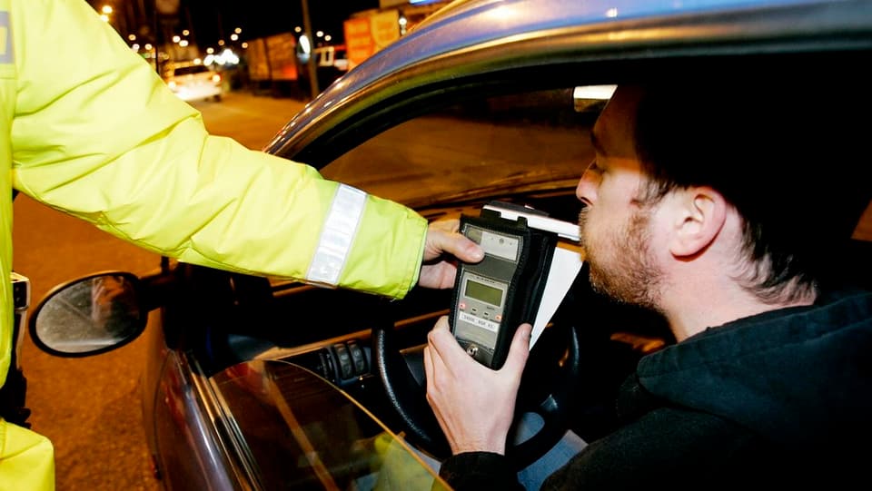 Ein Mann hinter dem Steuer eines Autos bläst auf Geheiss eines Polizisten in ein Promille-Testgerät